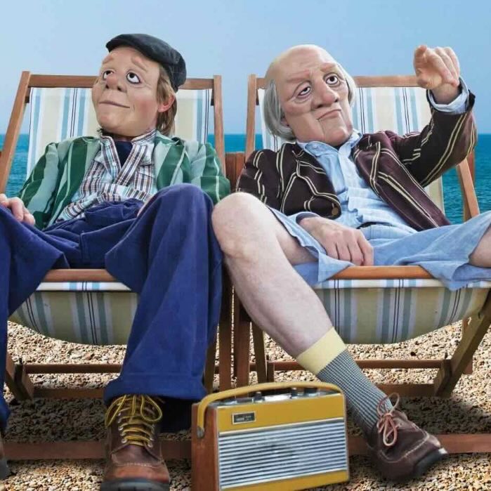 Two people sitting on deck chairs by the sea with a vintage radio between them.