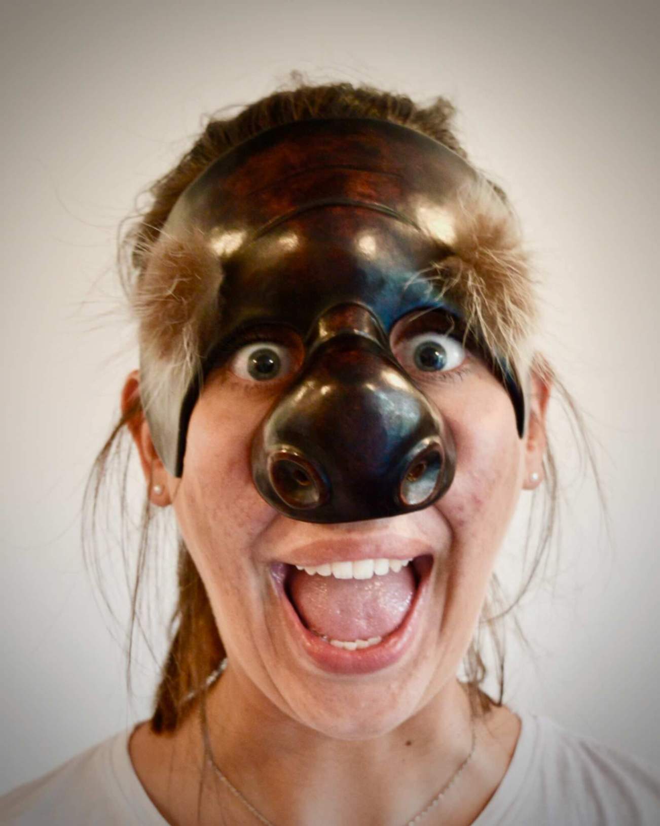 Person wearing an Il Dottore Commedia mask with a large nose and wide eyes on a plain background