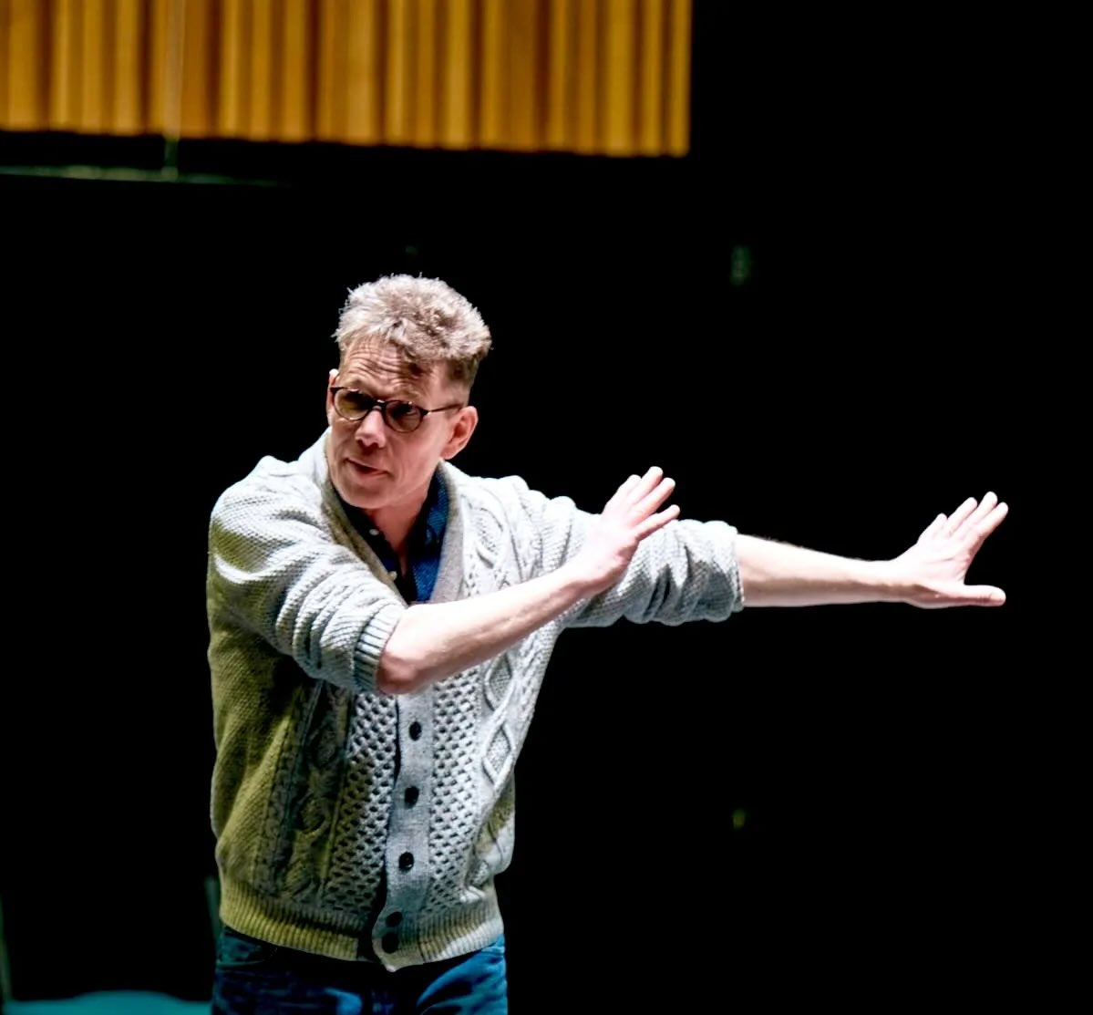Person wearing a light gray cardigan with arms outstretched against a dark background
